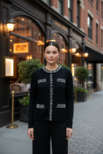 Load image into Gallery viewer, Woman wearing a black sweater with white patterns on a city street.