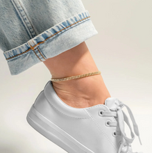 Load image into Gallery viewer, White sneaker worn with rolled-up jeans and a gold anklet on a neutral background